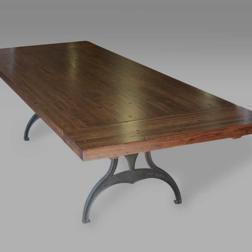 A sturdy wooden table with a dark finish and thick top sits on black metal pedestal legs, great for industrial decor—all set against a neutral gray background.