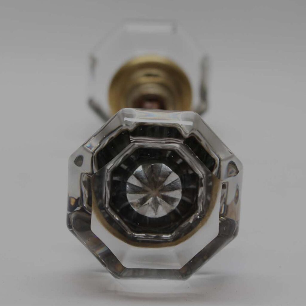 Two vintage glass doorknobs with faceted surfaces and brass centers sit against a plain backdrop. Chrome hardware frames the knobs, adding elegance, suitable for DIY home projects or restoration.