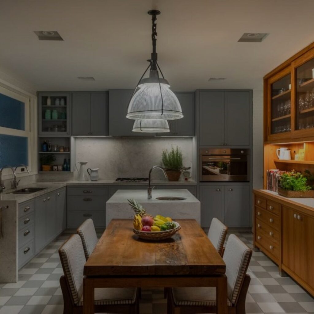 Modern kitchen with gray cabinets, wooden dining table, and pendant lighting.