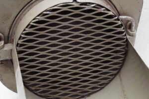 Gray metal industrial traffic light shown in close-up with a circular diamond-pattern grille.