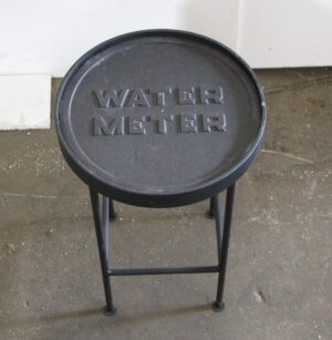 Round side table with a reclaimed water meter cover top and a simple metal base, shown from above.