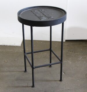 Round side table with a cast iron meter cover top and four slim metal legs.