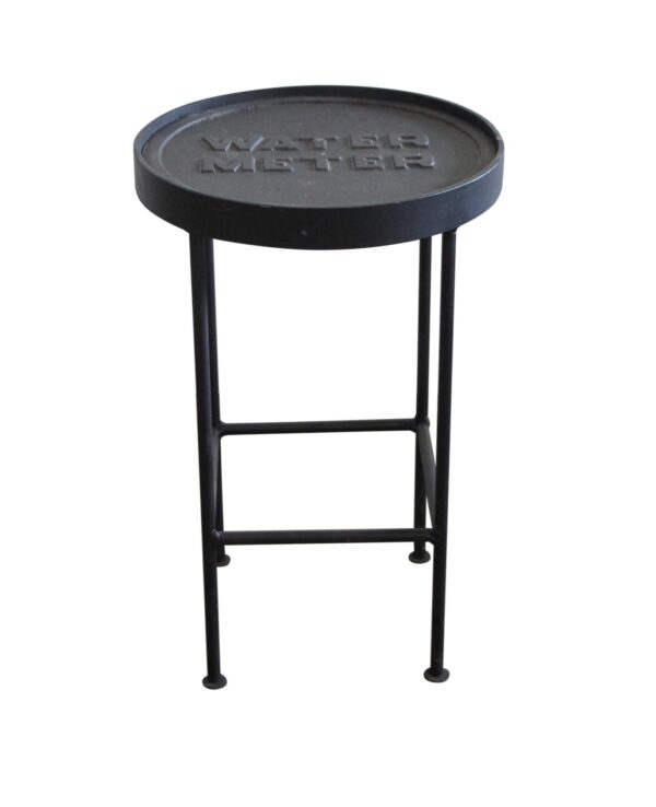 Round side table with a cast iron water meter cover top and slender metal legs, shown in a front view.