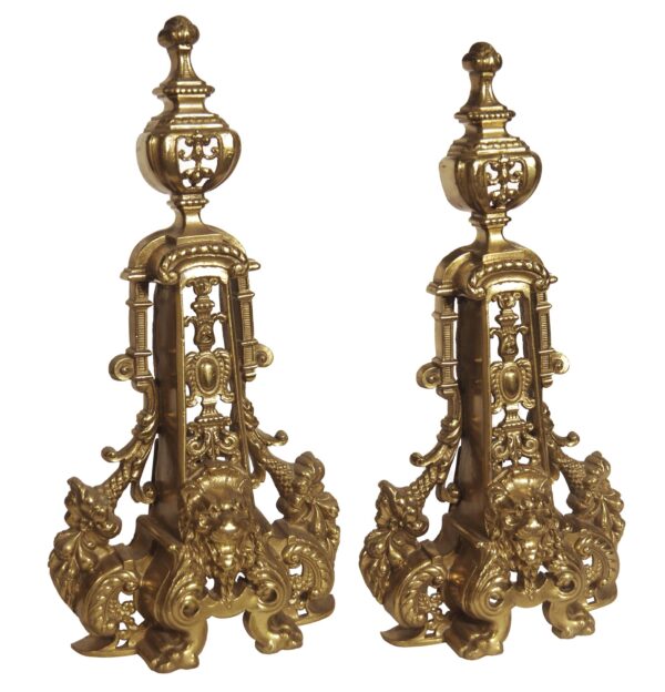 Pair of polished brass chenets with ornate French styling and lion head details, shown as a matching pair.