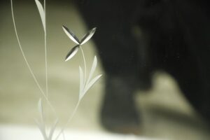 Close-up of a beveled etched wall mirror with floral details, showing the decorative vine pattern and a chipped corner.