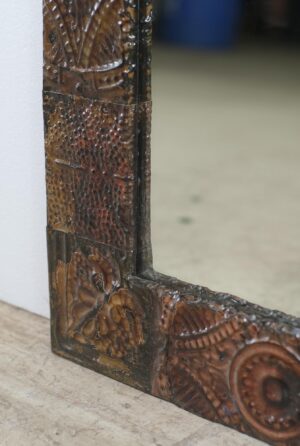 Close-up of a wall mirror with a brown handcrafted frame made from mixed-pattern antique tin ceiling tiles.