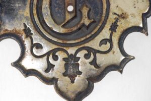 Metal applique with a tulip design and a letter D cutout, shown in close-up with a worn silver finish and dark edging.