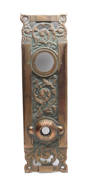 Ornate antique bronze entry back plate with floral scrollwork, a large circular opening, and mounting holes at the top and bottom.