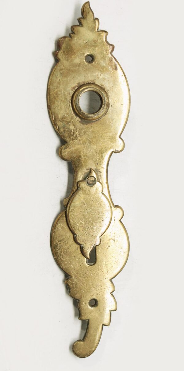 Antique brass door back plate with an extra long keyhole cover, shown front on with surface wear and decorative cutouts.