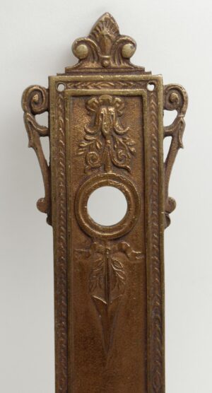 French-style bronze door back plate with a central keyhole opening and ornate floral detailing.