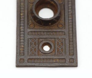 Ornate cast iron door back plate with Aesthetic design and two keyhole openings, shown in a close-up view.
