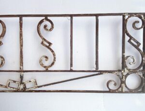Antique wrought iron window guard or transom with scrollwork and vertical bars, shown in a rusted black finish.