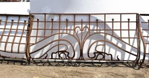Art Nouveau wrought iron balcony with a central panel and curved side extensions, shown in a front view with decorative scrollwork and arched top details.