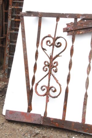 Heavily rusted wrought iron fire escape balcony front with ornate scrollwork and bent frame sections.