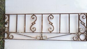 Antique wrought iron window guard with scrollwork and a rusted finish, shown as a rectangular panel.