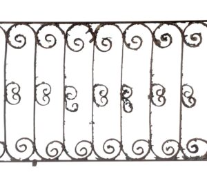 Wrought iron balcony railing section with curled scrollwork and vertical bars, shown front on with flaking paint and rust from age.