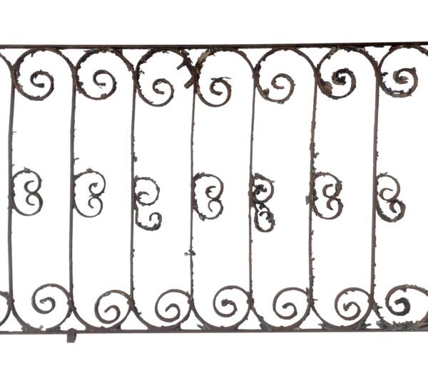 Wrought iron balcony railing section with curled scrollwork and vertical bars, shown front on with flaking paint and rust from age.