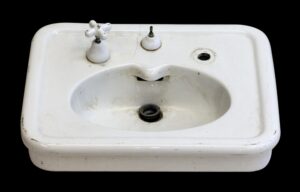 White porcelain sink with two cross handles, a center drain opening, and a hairline crack near the back center.