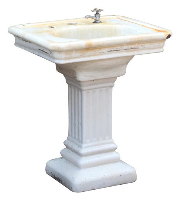 Pedestal sink with a fluted base and a single faucet hole, shown in white porcelain finish with visible chips and wear.