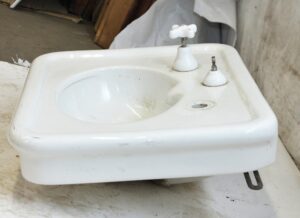 White porcelain sink with a rounded basin, two faucet openings, and a visible hairline crack near the back center.
