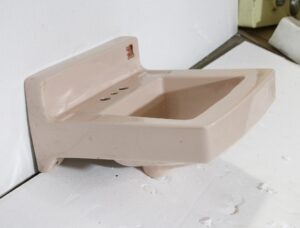 Pale pink porcelain sink with a rounded trapezoid bowl and side ledge, shown in a three-quarter view.