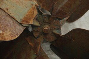 Close-up of an industrial fan blade with four curved blades and a rusty metal finish.