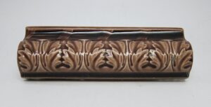 Brown ceramic cap tile with a vertical leaf pattern and visible age-related chips and scrapes.