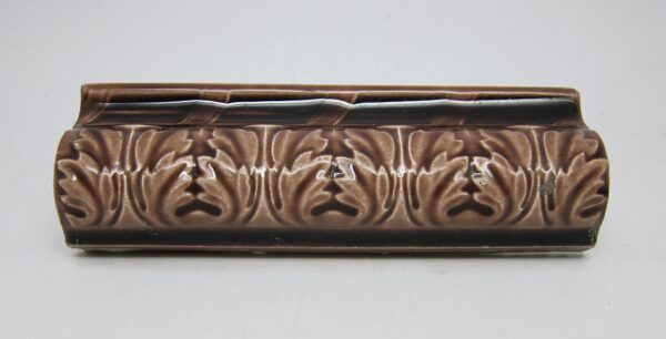 Brown ceramic cap tile with a vertical leaf pattern and visible age-related chips and scrapes.
