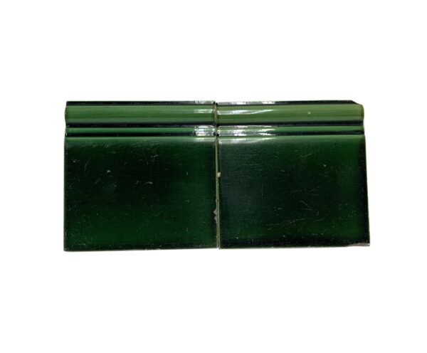 Pair of green ceramic baseboard tiles with a shiny crackled surface, shown side by side with visible chips and age-related wear.