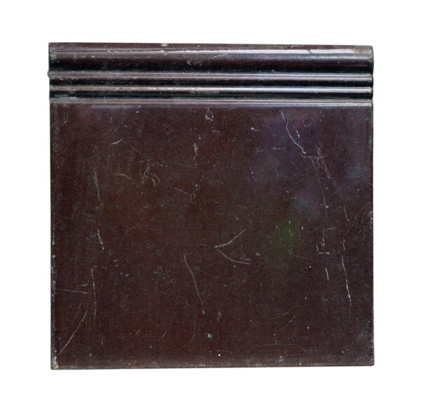 Brown ceramic wall baseboard tile with a molded top edge and visible age-related scratches and minor chips.