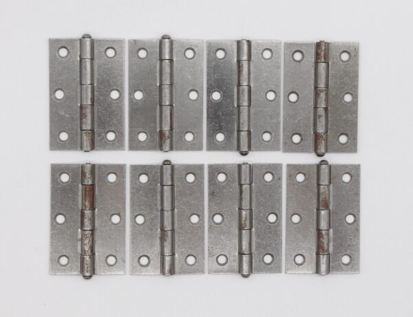 Set of eight steel butt cabinet hinges with five knuckles, rounded tips, and visible rust and age wear.