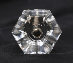 Clear hexagon glass cabinet knob with a central metal screw fitting, shown from the front on a dark background.