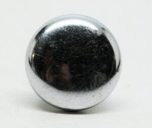 Chrome cabinet knob shown in close-up, with a rounded front and visible surface wear.