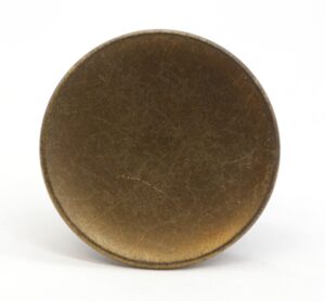 Round concave cabinet knob in antique brass finish, shown front on with visible surface wear and a centered mounting screw hole.