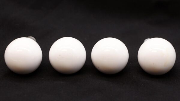 Four white ceramic ball cabinet knobs with brass shanks shown in a row, with minor staining visible on the surfaces.
