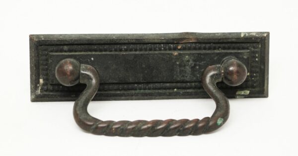 Traditional bronze bail drawer pull with a rectangular backplate and twisted handle, shown in a close-up view with some paint wear.