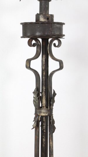 Close-up of a wrought iron floor candelabra lamp with scrollwork and foliate details, showing the upper stem and part of the five-light structure.