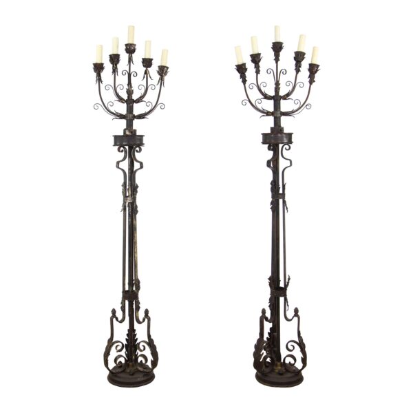 Pair of wrought iron floor candelabra lamps with five lights each, shown as a matching pair with foliate details and ornate scroll bases.