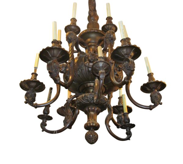 Antique brass 18-arm chandelier with a multi-tiered French design, showing scrolled arms, cherub head details, scalloped bobeches, and candelabra sockets with ivory-colored sleeves.