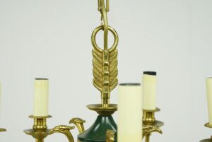 Close-up of a French Empire chandelier with an antique brass leaf detail, a green central accent, and visible candle-style arms with candelabra sockets.
