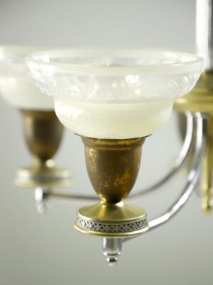 Close-up of a chandelier slip shade made of clear and frosted glass with a nickel and antique brass fixture visible beneath it.