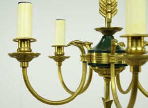 Close-up of a French Empire chandelier with brass arms, eagle-head details, and green center accents.