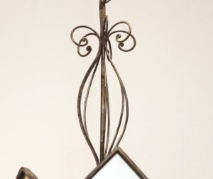 Close-up of a wrought iron chandelier with scrollwork and a mirrored glass panel, showing the upper section and one angled panel.