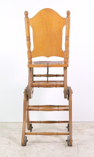 Front view of a vintage convertible children's chair with wheels, showing the high chair and stroller configuration in a light wood tone with wicker seat and wooden frame.