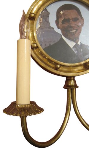 Brass wall sconce with a circular picture frame and one visible candle-style bulb holder.