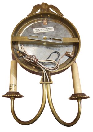 Round brass wall sconce with two curved arms and an eagle motif at the top, shown from the back with visible wiring and mounting hardware.