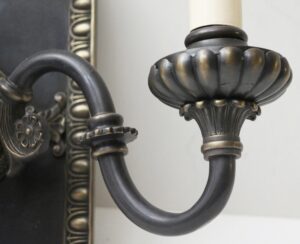 Close-up of a Tudor-style wall sconce arm with a fluted metal candle cup in black and gold finish.