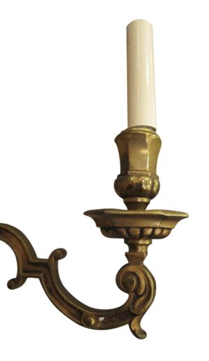 Close-up of an Empire-style wall sconce with a single candle sleeve and ornate curved bronze arm with gilt finish.
