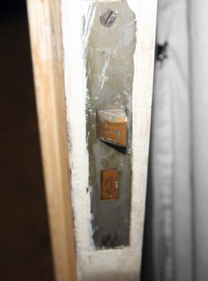Close-up of a closet door edge showing the latch plate and strike hardware on the white-painted mirrored side.