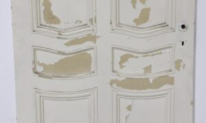 Distressed white six-panel door with curved molding and flaking paint around the knob and keyhole area.